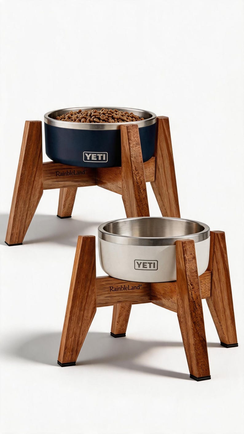 May include: Two elevated pet bowls featuring stainless steel interiors and coloured exteriors, one navy blue and one white, each branded with the YETI logo. The bowls are held by wooden stands labelled RainbleLand with four angled legs and black feet.