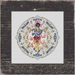 May include: A cross-stitch design featuring a blue figure playing a flute, adorned with a crown and jewelry. The figure is set against a detailed, circular mandala with floral and geometric patterns. The artwork is framed in a dark, textured wooden border.