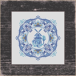 Può includere: Un disegno a punto croce con un mulino a vento blu e motivi floreali. Il mulino a vento è centrato all'interno di una cornice circolare, circondato da intricati motivi floreali blu e gialli. L'opera d'arte è su uno sfondo chiaro e incorniciata in legno scuro.