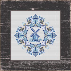 May include: Cross-stitch design of a blue windmill in a circular frame, with floral and geometric patterns in blue and yellow. The artwork is set against a light background and framed in a dark, distressed wood.