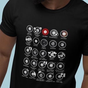 May include: Black t-shirt featuring a grid of vinyl record illustrations with various designs and text. The text includes phrases like "Vinyls are cool," "Different sizes," and "They sound good." The shirt is a music-themed apparel item.