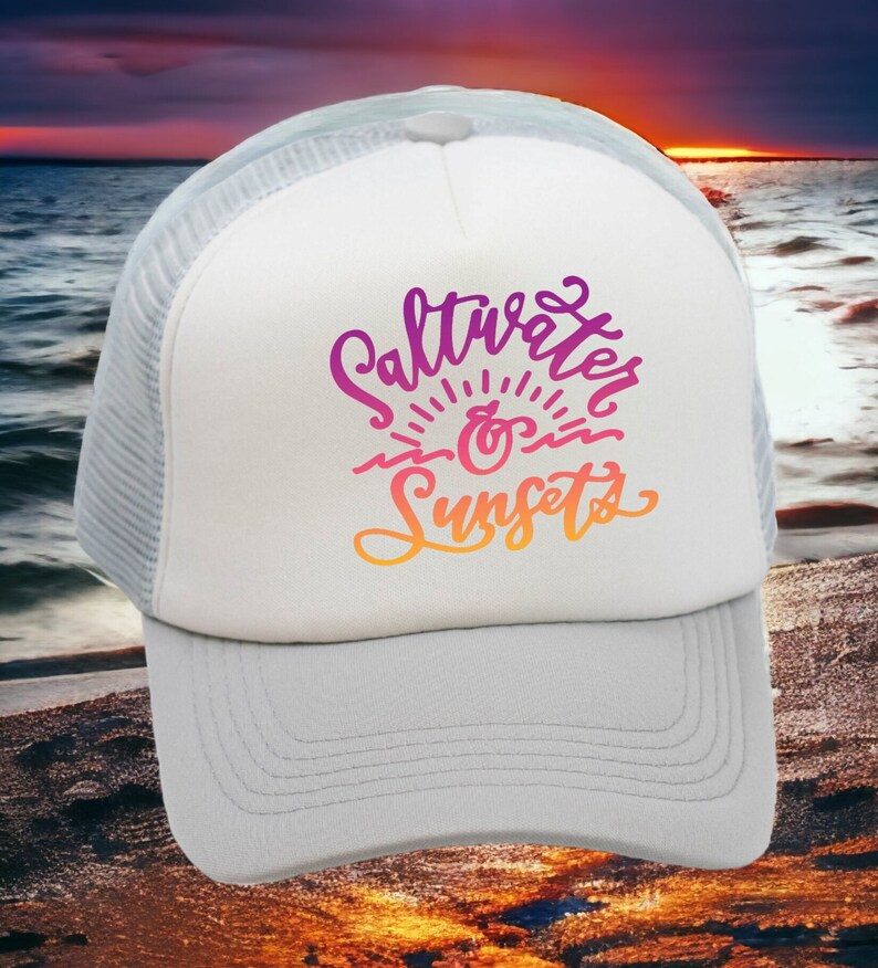 May include: White trucker hat with a mesh back. The front of the hat has a pink, orange, and yellow graphic that says "Saltwater & Sunsets".