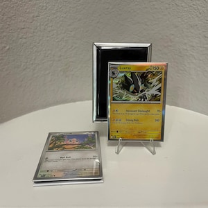 Puede incluir: Dos cartas coleccionables de Pok&eacute;mon, una con Luxray y otra con un Jigglypuff. La carta de Luxray es amarilla y negra, expuesta en un soporte transparente. Un espejo con marco negro est&aacute; detr&aacute;s de la carta de Luxray. La carta de Jigglypuff es plateada y rosa.