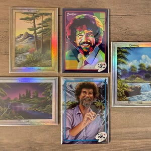 Puede incluir: Cinco impresiones art&iacute;sticas enmarcadas con pinturas de paisajes y retratos de Bob Ross. Las impresiones tienen un borde plateado y un efecto hologr&aacute;fico. Un retrato muestra a Bob Ross con un pincel, y otro es de estilo pop art colorido.