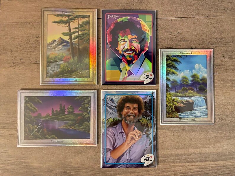 Puede incluir: Cinco impresiones art&iacute;sticas enmarcadas con pinturas de paisajes y retratos de Bob Ross. Las impresiones tienen un borde plateado y un efecto hologr&aacute;fico. Un retrato muestra a Bob Ross con un pincel, y otro es de estilo pop art colorido.