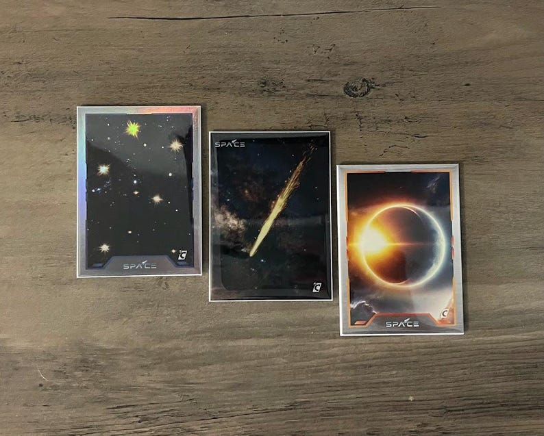 Puede incluir: Tres cromos con im&aacute;genes espaciales. Uno muestra un cielo estrellado, otro un cometa y el tercero un eclipse solar. Cada cromo tiene la palabra "SPACE" y un n&uacute;mero.