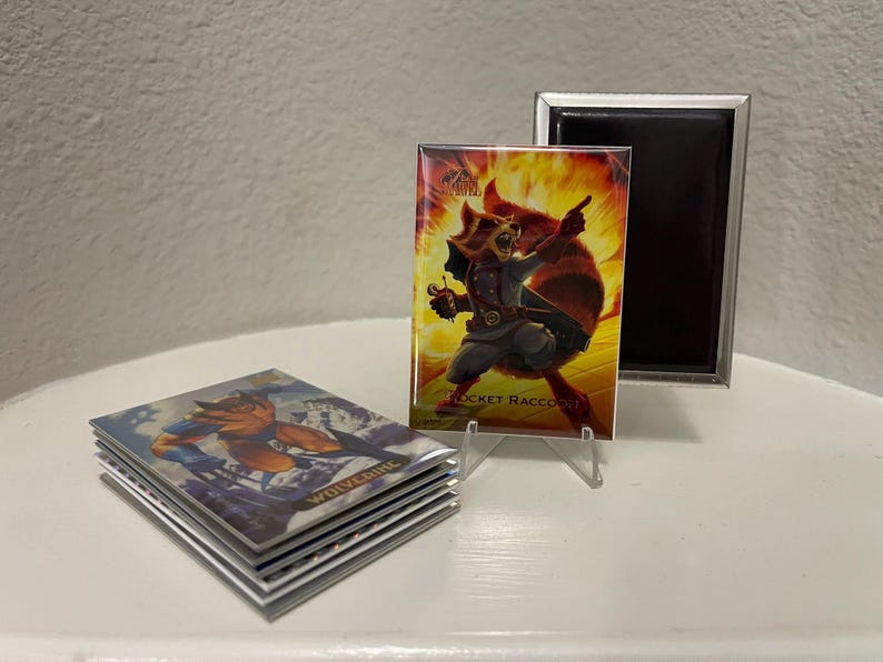 Puede incluir: Una pila de cromos con Wolverine y una tarjeta de Rocket Raccoon en exhibici&oacute;n. La tarjeta de Rocket Raccoon est&aacute; en un soporte transparente, con un marco magn&eacute;tico negro detr&aacute;s. La tarjeta de Rocket Raccoon tiene un fondo ardiente.