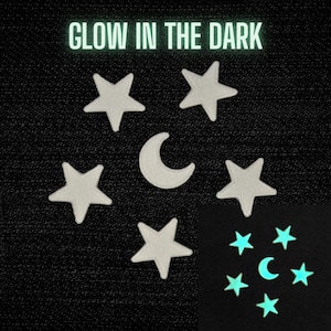 May include: White star and crescent moon patches on a black background. The text "GLOW IN THE DARK" is at the top. A smaller image shows the patches glowing in the dark, with a teal colour.