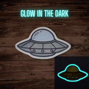 May include: Embroidered patch featuring a gray and light blue UFO design with the text "GLOW IN THE DARK". The patch has a white border and a smaller image showing the glow-in-the-dark effect.