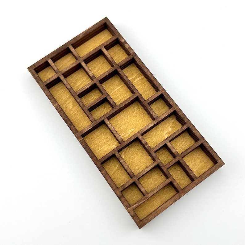 May include: A rectangular wooden organizer tray featuring a dark brown frame and a light tan interior base. The tray is divided into multiple compartments of varying sizes and shapes, creating a grid-like structure for sorting and storage.