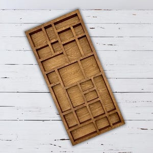 May include: A rectangular wooden organizer with various sized compartments. The organizer is made of light brown wood and has a grid-like pattern of rectangular and square spaces. The wood grain is visible, and the organizer is set against a white wooden background.