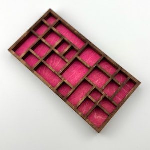 May include: A rectangular wooden organizer tray featuring a dark brown wood frame and a vibrant hot pink interior base. The tray is divided into multiple compartments of varying sizes and shapes, creating a grid-like structure for storage.