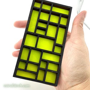 May include: A rectangular wooden grid structure featuring a black frame with multiple internal compartments. Each individual section is filled with a vibrant, solid lime green backing, creating a high-contrast geometric pattern throughout the piece.