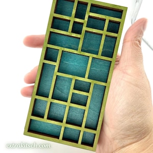 May include: A rectangular wooden grid display piece featuring a light green frame and deep teal blue interior compartments. The structure consists of various sized rectangular and square openings arranged in an asymmetrical pattern. Text reads extrakitsch.com.