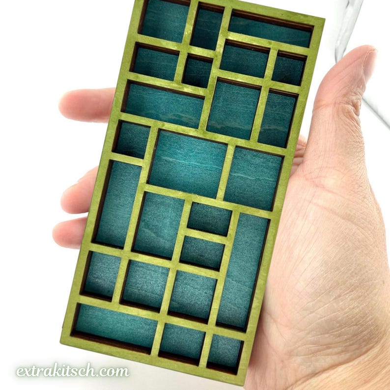 May include: A rectangular wooden grid display piece featuring a light green frame and deep teal blue interior compartments. The structure consists of various sized rectangular and square openings arranged in an asymmetrical pattern. Text reads extrakitsch.com.