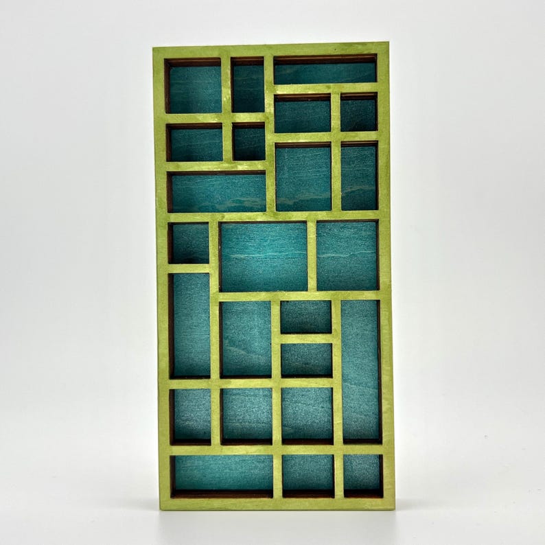 May include: A rectangular wooden display shelf featuring a grid of various sized compartments. The outer frame and internal dividers are painted in a light lime green, while the back panel of each individual section is a deep teal blue color.