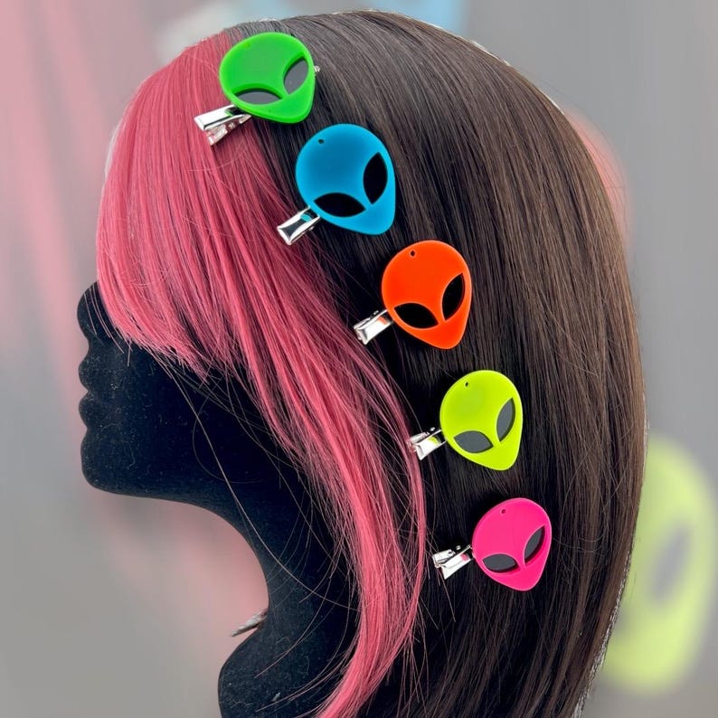 Op de afbeelding: Een set van zes kleurrijke haarclips in de vorm van aliens. De clips zijn gemaakt van plastic en hebben een glanzende afwerking. De kleuren van de clips zijn groen, blauw, oranje, geel, roze en limoengroen.