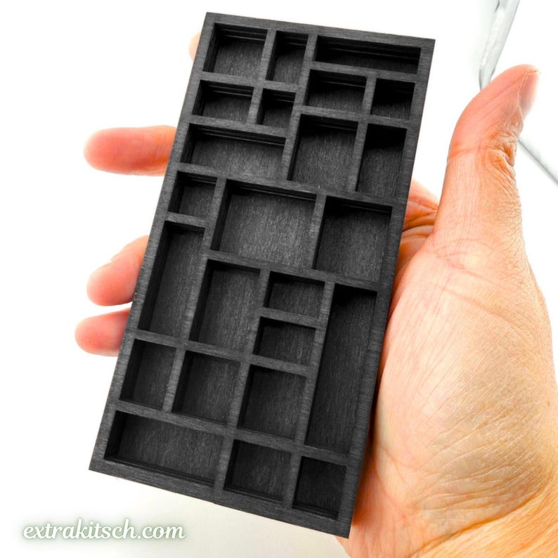 May include: A rectangular black wooden display shelf featuring multiple compartments of varying sizes arranged in a grid pattern. The structure has a flat surface with raised dividers creating individual open sections for storage or display purposes.