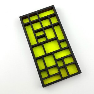 May include: A rectangular grid panel featuring a dark charcoal wooden frame with a series of intersecting horizontal and vertical dividers, creating various open rectangular compartments that reveal a bright neon yellow backing.