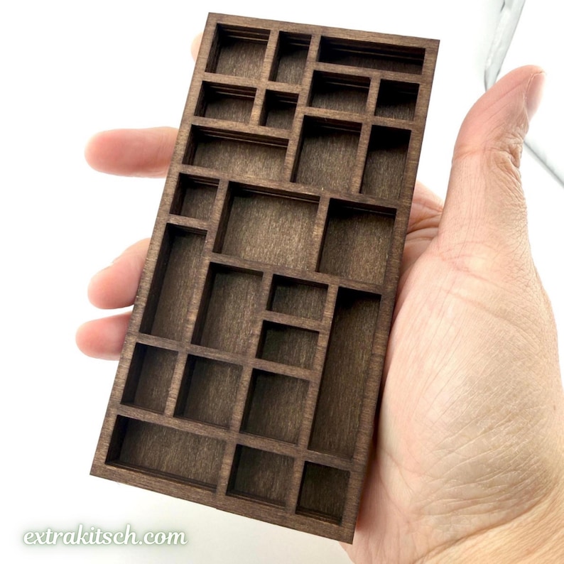 May include: A rectangular dark brown wooden display shelf featuring multiple compartments of varying sizes arranged in a grid pattern. The item has a smooth finish and is constructed with thin dividers, creating a structured layout for small items.