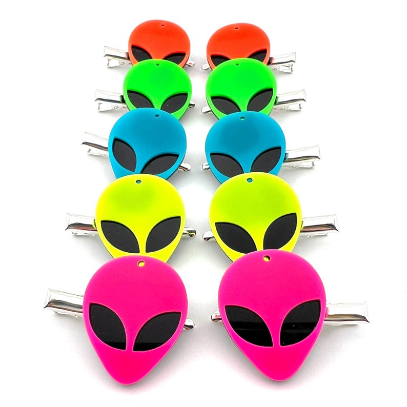 Op de afbeelding: Set van tien neon alien-hoofd haarclips. De clips zijn in verschillende kleuren, waaronder groen, blauw, geel, roze en oranje. Elke clip heeft een zwart alien-hoofd met grote ogen.