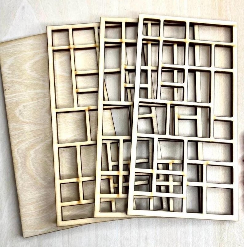 May include: Three rectangular light-colored wooden panels featuring a laser-cut grid pattern of various sized open squares and rectangles. The panels are stacked slightly offset, revealing the natural wood grain and smooth, light brown edges.