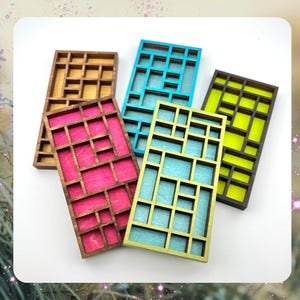 May include: Five wooden trays with different colored backgrounds and a grid pattern. The trays are in shades of brown, pink, blue, green, and black.