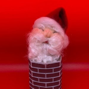 Op de afbeelding: Een witte baard kerstmanpop met een rode muts zit vast in een bakstenen schoorsteen. De schoorsteen is gemaakt van bruine en zwarte bakstenen.