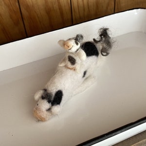 May include: A white and black felted cow with a smaller white and black felted calf riding on its back.