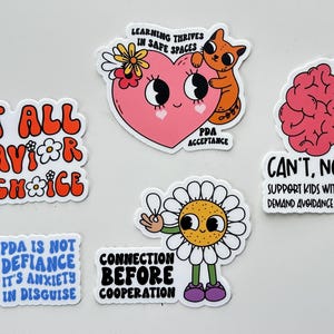 May include: A collection of colorful stickers with various designs and text. One sticker reads "Not All Behavior Is A Choice." Another features a pink heart with a cat and the text "Learning Thrives in Safe Spaces." Other stickers include a brain, daisy, and text.