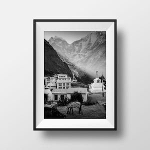 Puede incluir: Una fotografía en blanco y negro de un pueblo de montaña en el Himalaya. El pueblo está enclavado en un valle rodeado de montañas cubiertas de nieve. Una estupa blanca se alza en primer plano, con un caballo pastando cerca.