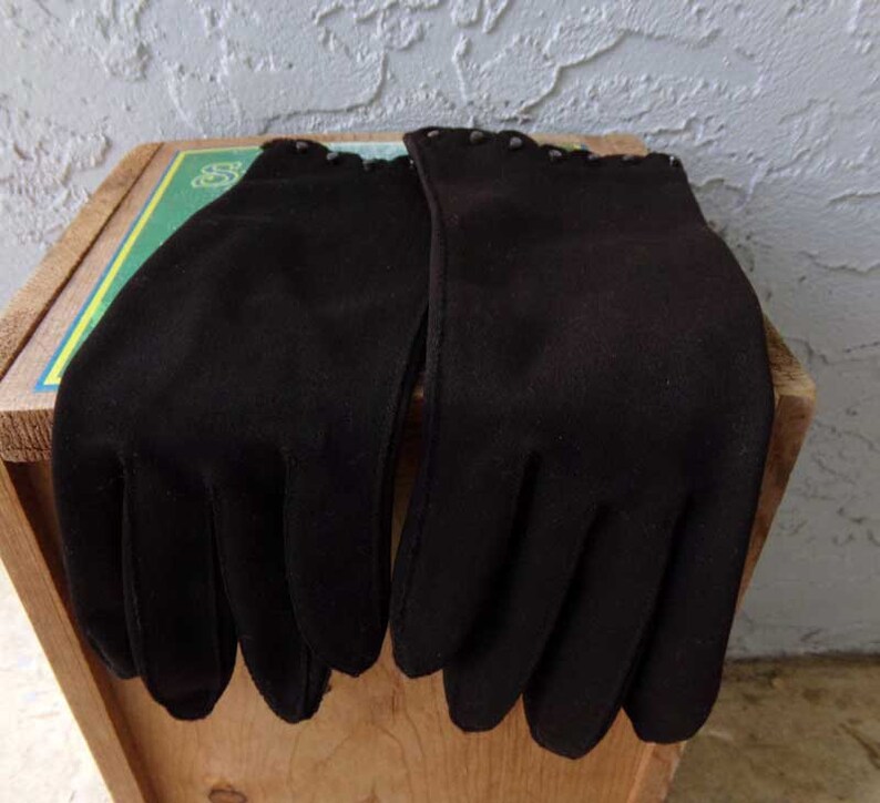 Pode incluir: Um par de luvas pretas com uma guarni&ccedil;&atilde;o decorativa em torno do pulso.