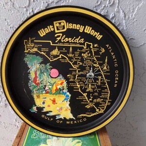 May include: A black metal tray with a gold rim featuring a map of Florida with the text "Walt Disney World Florida" and "Atlantic Ocean" and "Gulf of Mexico". Mickey Mouse and other Disney characters are depicted on the beach.