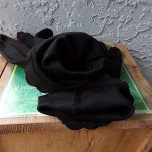 Pode incluir: Um par de luvas pretas dobradas e dispostas em forma de rosa sobre uma superf&iacute;cie de madeira com fundo verde e amarelo.