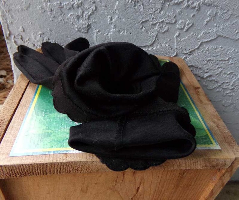 Pode incluir: Um par de luvas pretas dobradas e dispostas em forma de rosa sobre uma superf&iacute;cie de madeira com fundo verde e amarelo.