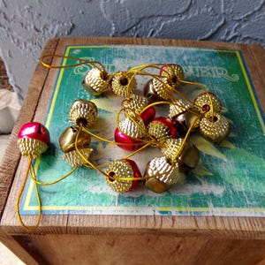 May include: A collection of small, decorative acorn ornaments. The acorns have a metallic gold base and a red or gold cap. They are strung together with gold string, perfect for holiday decorations.