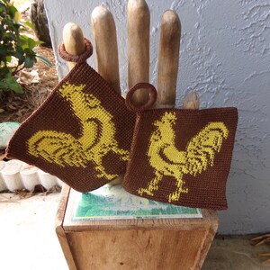 May include: Two brown crocheted pot holders with yellow rooster designs. The pot holders have loops for hanging.