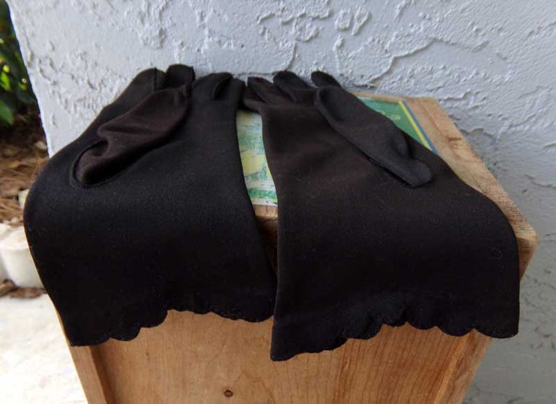 Pode incluir: Dois pares de luvas pretas de comprimento do cotovelo com bordas festoneadas.