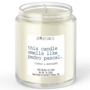 May include: A clear glass jar candle with a white label that reads "this candle smells like pedro pascal." The label also includes the text "JENJUTE CANDLE CO", "CITRUS & WOODLAND", "100% NATURAL SOY CANDLE", "NET WT. 7oz (200g)", and "HAND-POURED IN SOUTHWEST VIRGINIA, USA".