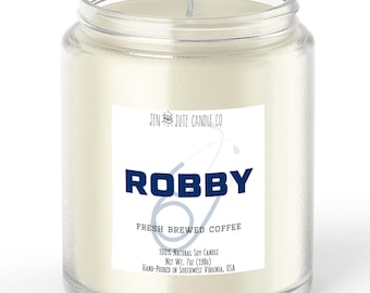 May include: A clear glass jar candle with a white label. The label reads "ROBBY FRESH BREWED COFFEE" in blue text. The candle is 7 oz (198g) and made of 100% natural soy wax. The text "JEN AND JUTE CANDLE CO" is also visible.