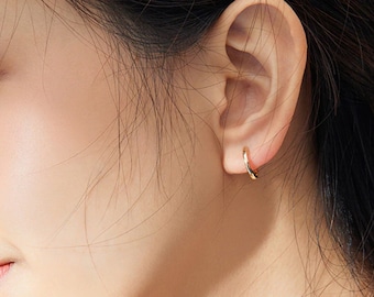 May include: A close-up of a person's ear with a small gold hoop earring. The earring is simple and elegant, and it would be a great addition to any jewelry collection.