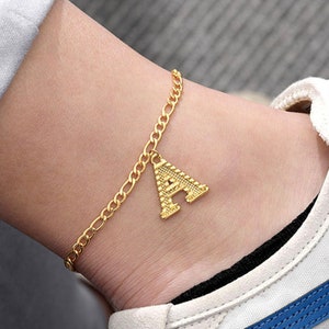 Peut inclure: Chaîne de cheville dorée avec un pendentif en forme de lettre A. La chaîne est de style curb et le pendentif est texturé.