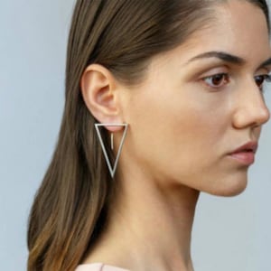 May include: Silver triangle earrings with a dangling drop. The earrings are geometric and modern in style.