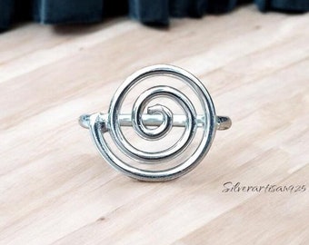 Puede incluir: Un anillo de plata con un diseño en espiral. El anillo está sobre una superficie de madera.