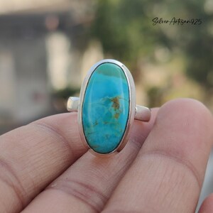 May include: A silver ring with a large oval turquoise stone. The stone is a vibrant blue with brown veins.