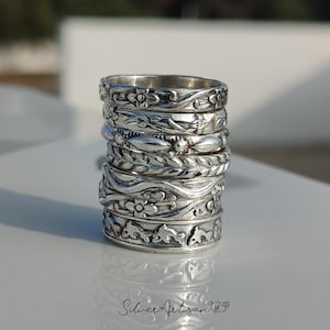 May include: A collection of silver rings featuring detailed floral and leaf patterns. The rings are stacked, displaying the intricate designs. The rings are made of a shiny, metallic material, reflecting light.