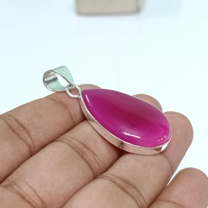 May include: A silver pendant featuring a teardrop-shaped pink agate gemstone. The pendant is set in a silver bezel and has a silver bail.