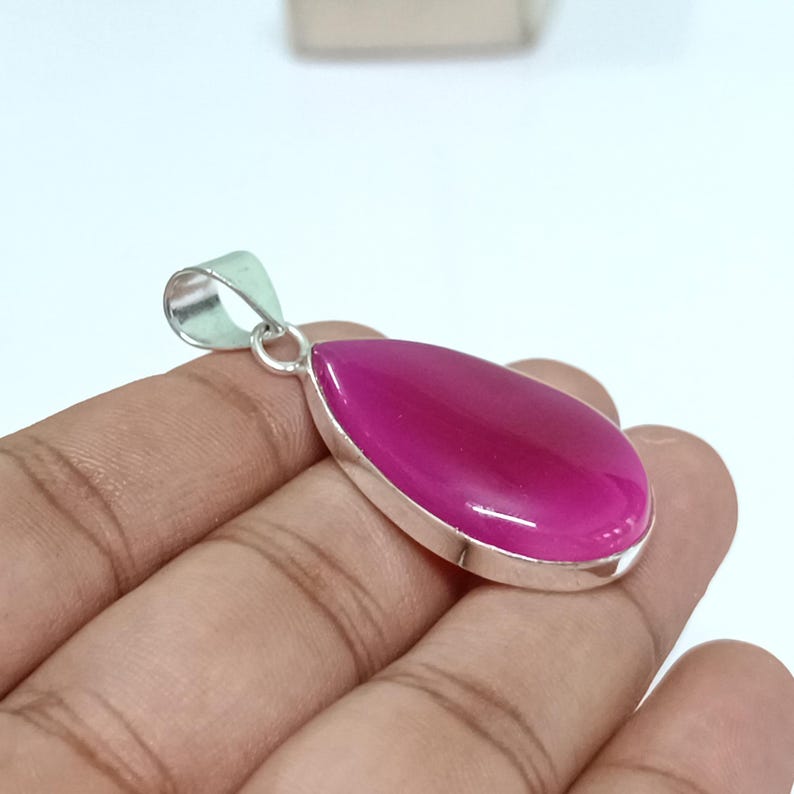 May include: A silver pendant featuring a teardrop-shaped pink agate gemstone. The pendant is set in a silver bezel and has a silver bail.