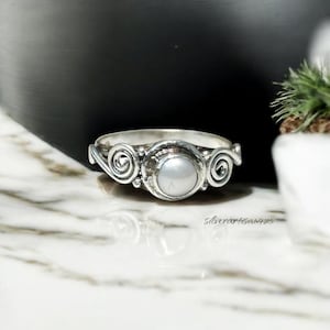 May include: A silver ring with a white pearl set in a swirl design.