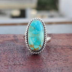 May include: A turquoise ring with a silver band and a rope-like design. The turquoise is a light blue color with brown veins.